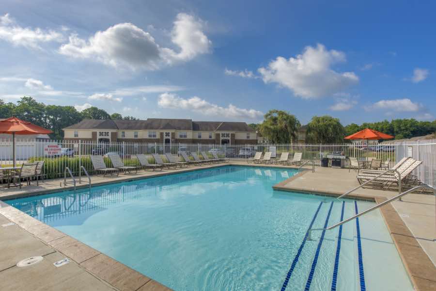 Plan ahead and get to your apartment without delay so you can enjoy amenities like this swimming pool at Ashley Place. Apartment swimming pool with lounge chairs and tables with umbrellas
