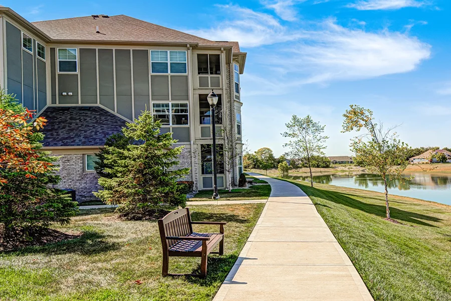 Suburban apartments like Harmony Apartments are more likely to have green space and a view. A view of an apartment building and bench looking out over a retention pond at Harmony Apartments